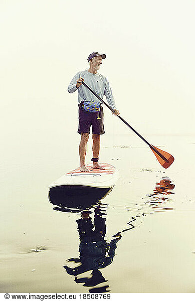 A mature man standup paddle boarding on an early foggy morning