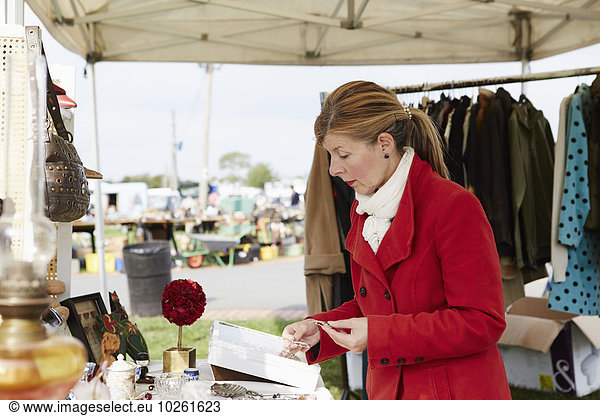 A mature woman bargain hunter browsing through vintage jewellery items at a clothing stall at a flea market.