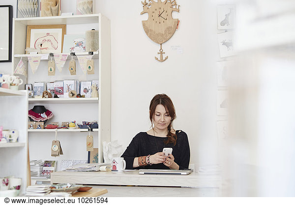 A mature woman sitting using a smart phone in a gift shop  running a small retail business.