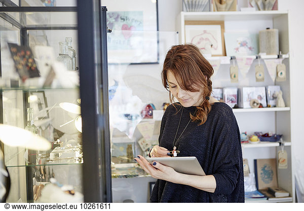 A mature woman using a digital tablet  using the touch screen  stock-taking in a small gift shop.