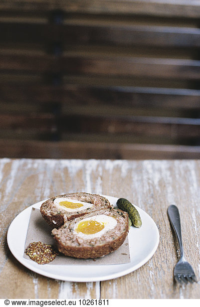 A meal on a plate  a scotch egg cut in half with garnishes.