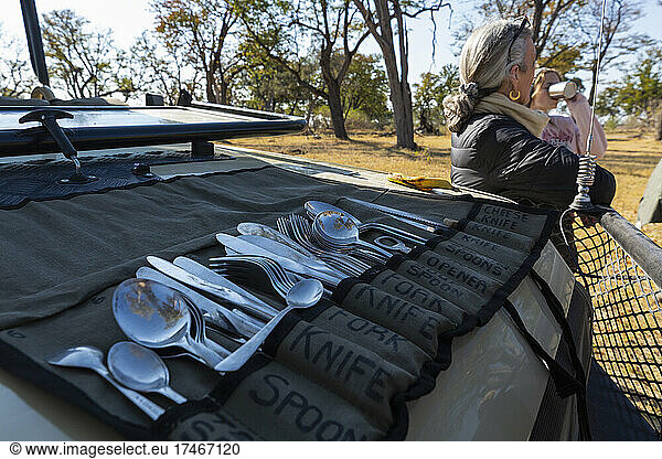 A meal stop on safari  people having drinks  and a roll of cutlery spread on the dashboard of a safari vehicle