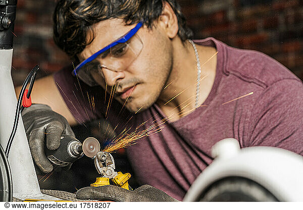 A mechanic wearing safety goggles using a mini grinder to cut a screw