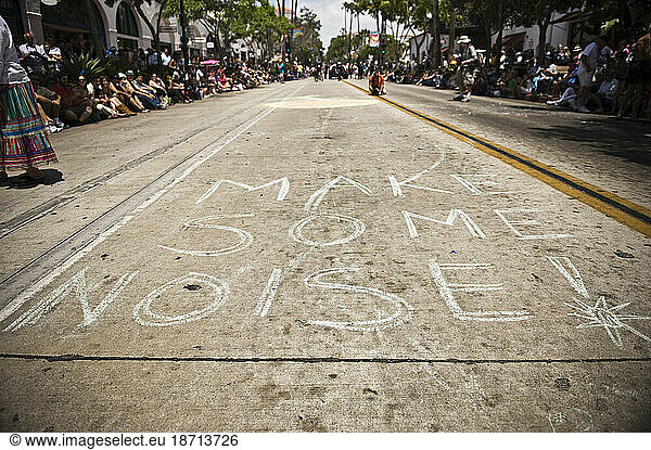 A message in chalk at a parade in Santa Barbara. The parade features extravagant floats and costumes.