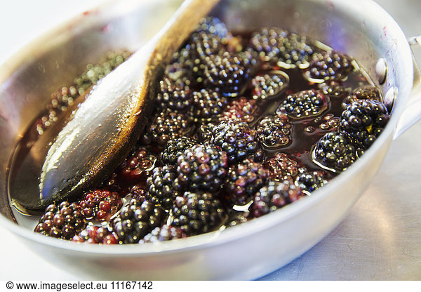 A metal dish of fresh blackberries  hedgerow berries  macerating in a liquid. Spoon.