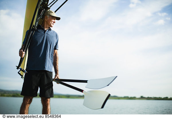 A middle-aged man carrying oars and a rowing shell on his shoulder.