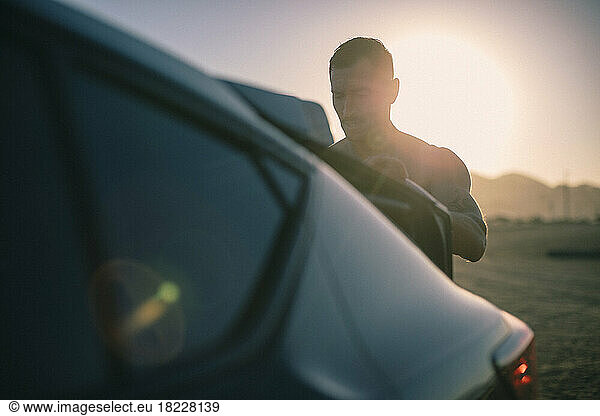 A middle aged man closes a trunk at sunrise.