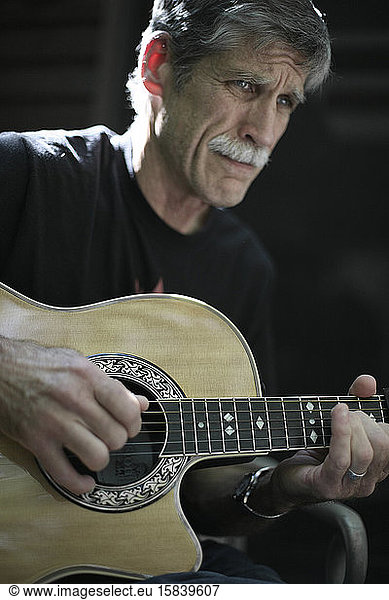 A middle aged man concentrating on playing guitar