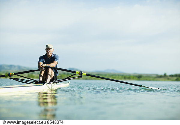 A middle-aged man rowing a single scull rowing boat on the water.
