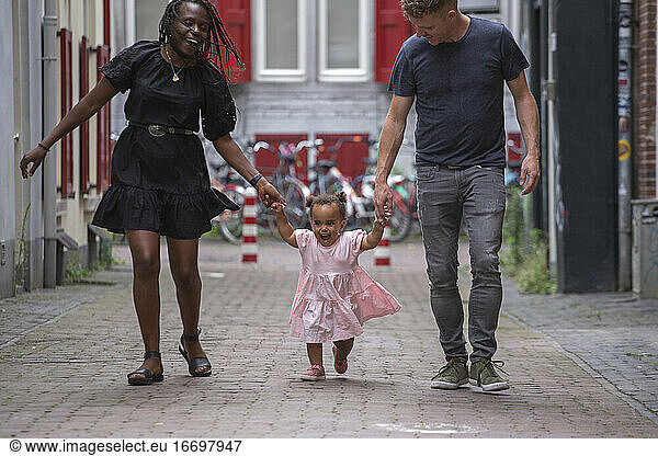 A mixed race family walking through the city with their young daughter