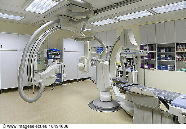 A modern hospital room  a large portable mobile scanning machine with curved shaped arms  a mobile scanner and hospital gurney or bed.