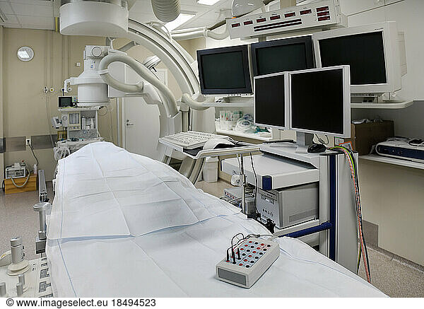 A modern hospital room  a large portable mobile scanning machine with curved shaped arms and banks of screens for medical imaging.