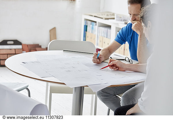 A modern office. Two people at a meeting discussing paper plans and using pens to draw and make amendments.