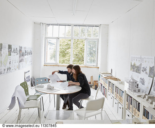 A modern office. Two people at a meeting discussing plans. Architectural drawings and building models.