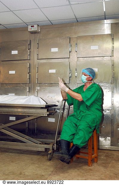 A mortuary technician adjusts his gloves  prior to inspecting a corpse.