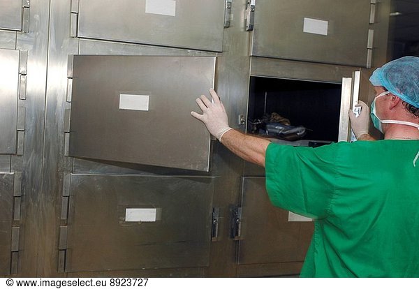A mortuary technician removes a human body from a cold storage facility.