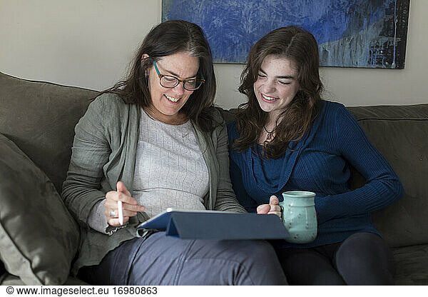 A mother and daughter smile while looking at a tablet together