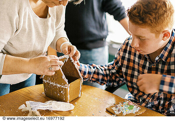 A mother and her children making a gingerbread house at dining table