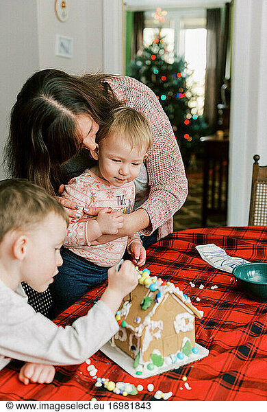 A mother and her children making a gingerbread house for the holidays