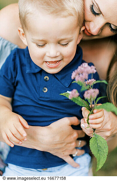 A mother and her son hugging lovingly and playing with a flower