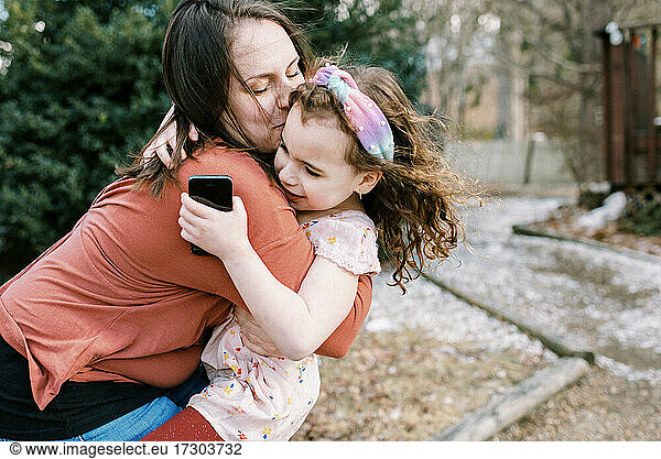 A mother holding and comforting her daughter holding cell phone