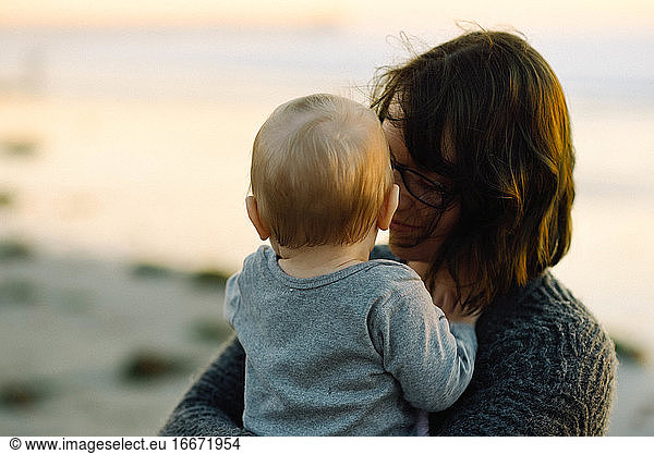 A mother holding her son lovingly during a sunset on the beach in cali