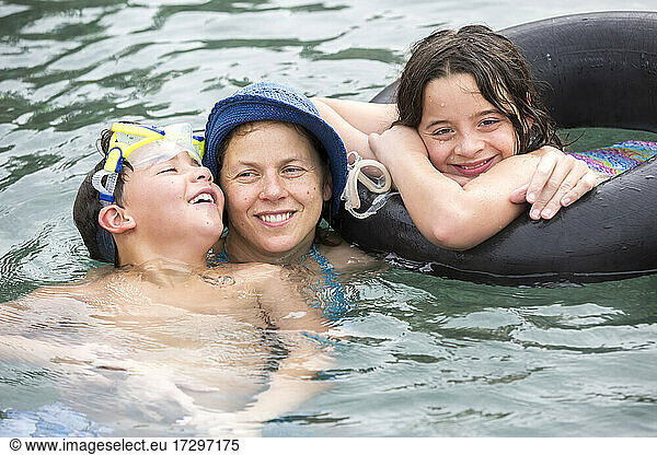 A mother hugs her two pre-teen children while floating in pool.