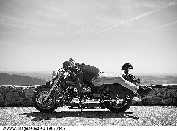 A motorcyclist enjoys the sunshine while taking a quick rest at an overlook.