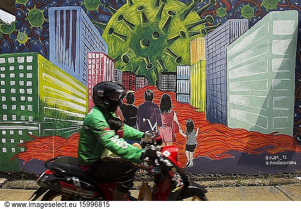 A motorcyclist passes in front of murals in Depok  West Java  which tells of a Coronavirus monster amid the city that killed tens of thousands of people during the Coronavirus (COVID-19) outbreak  April 16  2020.