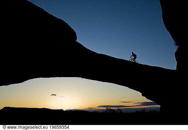 A mountain biker rides across a natural rock arch in the desert near Moab  Utah.