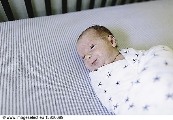 A newborn baby laying in his crib while swaddled