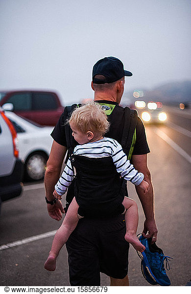 A one year old boy being carried in a baby carrier by his grandfather.