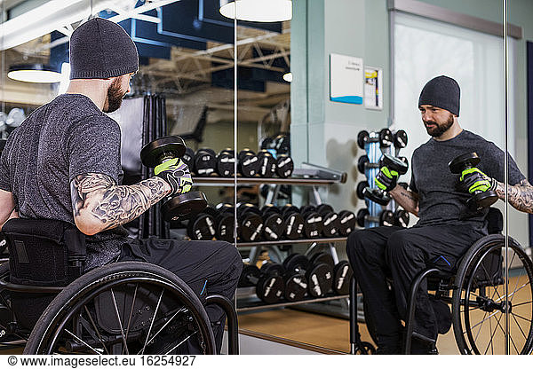 A paraplegic man working out using free weights in front of a mirror at recreational centre: Sherwood Park  Alberta  Canada