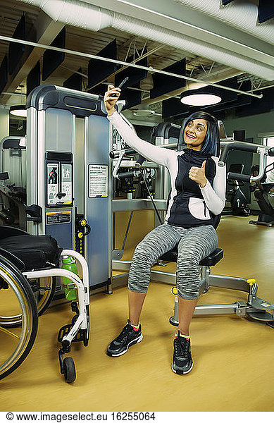 A paraplegic woman resting and taking a self-portrait after working out using an overhead press in a fitness facility; Sherwood Park  Alberta  Canada