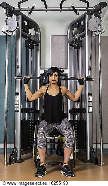 A paraplegic woman working out using a lat pull down machine in a fitness facility; Sherwood Park  Alberta  Canada