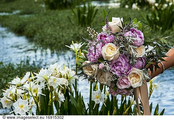 A partial view of a young woman holding a bouquet of flowers standing in a shallow river with wild Cahaba lillies in the background.
