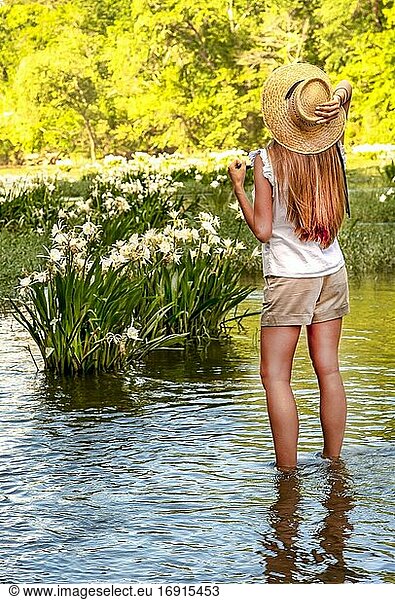 A partial view of a young woman standing in a shallow river with wild Cahaba lillies in the background.