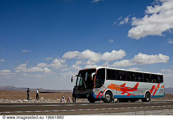 A passenger bus picks up two individuals on the side of the road in the Atacama Desert in Bolivia.