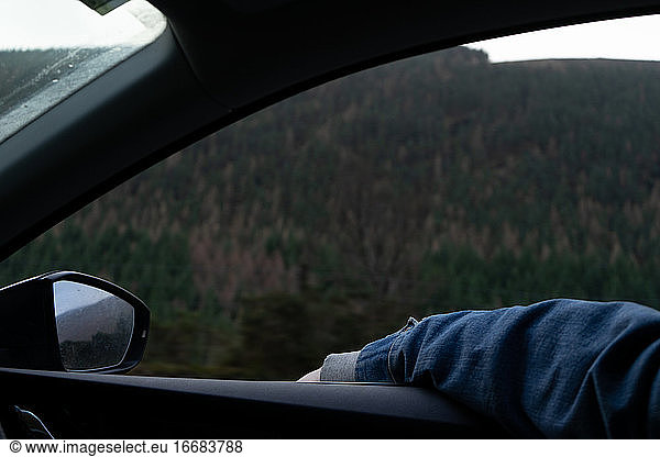 A passenger wearing a denim jacket leans their arm out the window