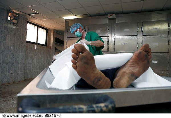A pathologist lifts the cover sheet from the body of a corpse in a mortuary.