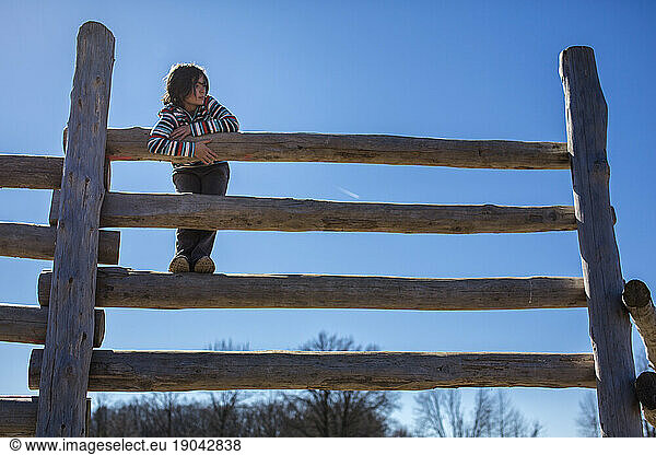 A peaceful child stands on a tall wooden fence in golden light looking