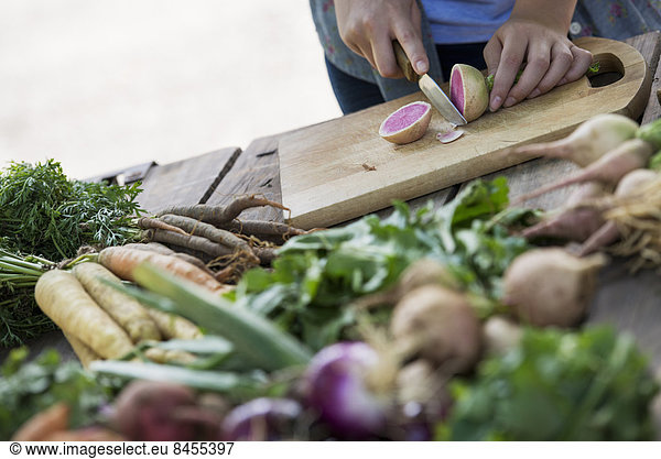 A person chopping freshly picked vegetables and fruits.