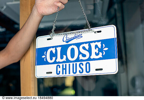 A person hanging up a sign on a restaurant door  reading Close. Closed  dual language  English and Italian.