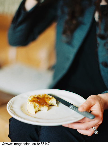 A person holding a plate  holding a half eaten scone with jam.