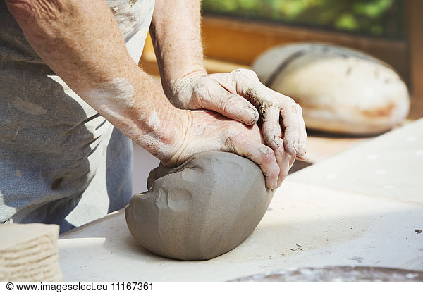 A person  potter preparing a lump of damp clay for throwing.