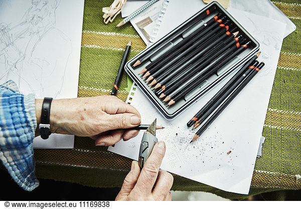 A person using a sharp blade  a craft knife  to sharpen lead pencils. Sketches on paper.