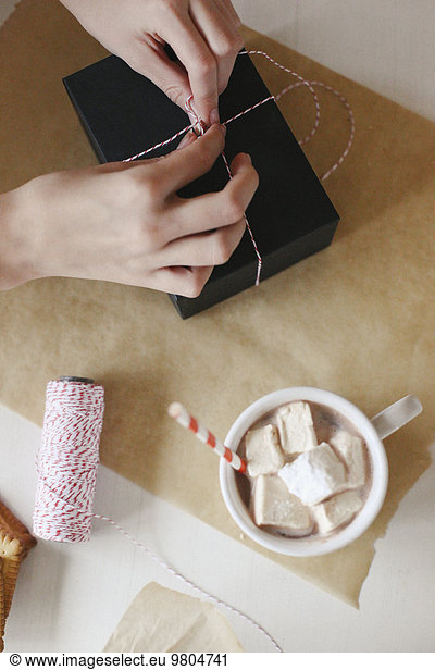 A person wrapping a parcel and a jar of homemade marshmallows.