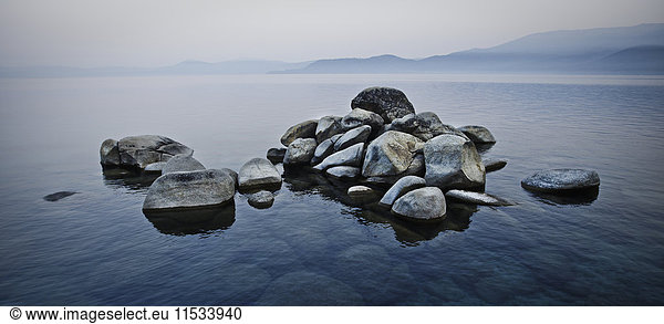 A pile of stones rising above the water level in a lake in a misty landscape.