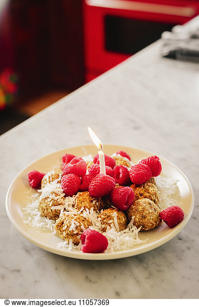 A plate with a dessert and fresh raspberries and a lit birthday candle.