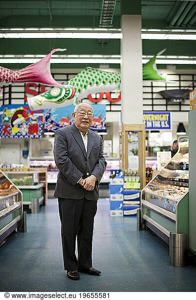 A portrait of an owner of a large grocery store standing in an aisle looking at the camera.